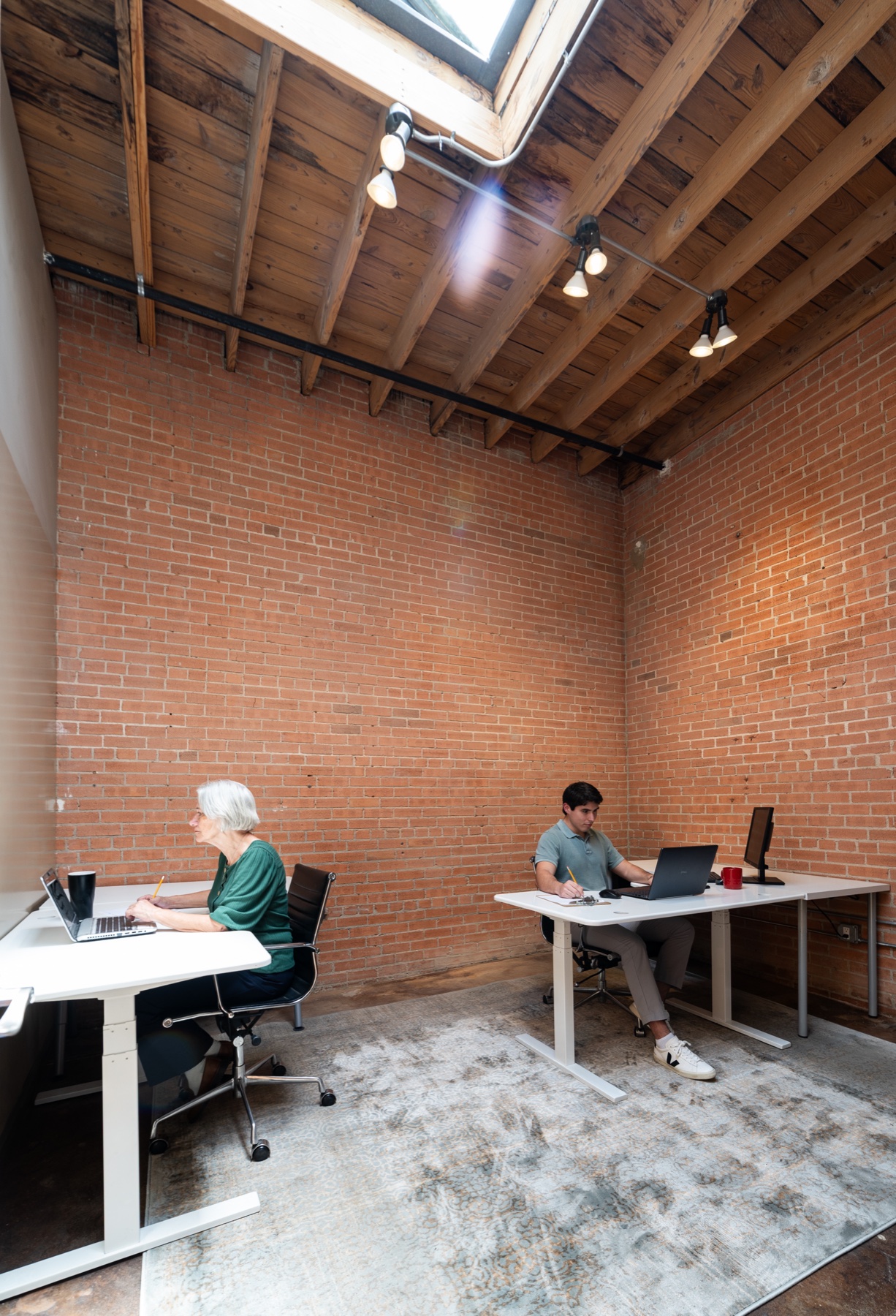 Two people working in a current brick-walled GeniusDen office